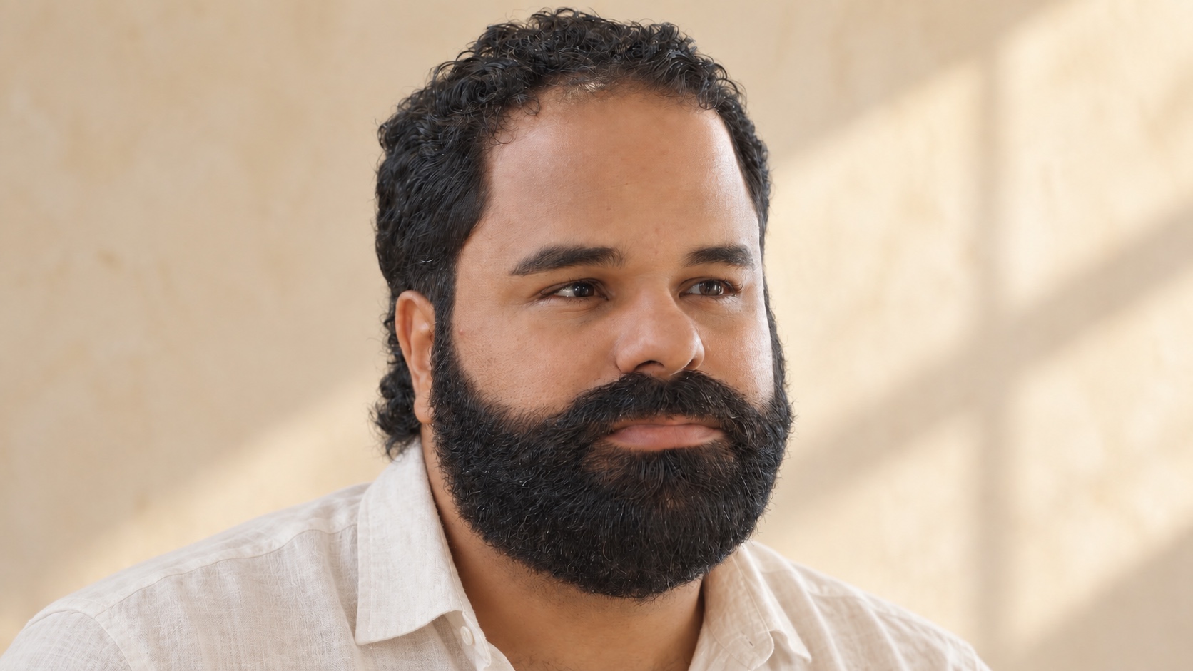 Barbú Origen portrait with natural curls and a relaxed expression in an ivory linen shirt